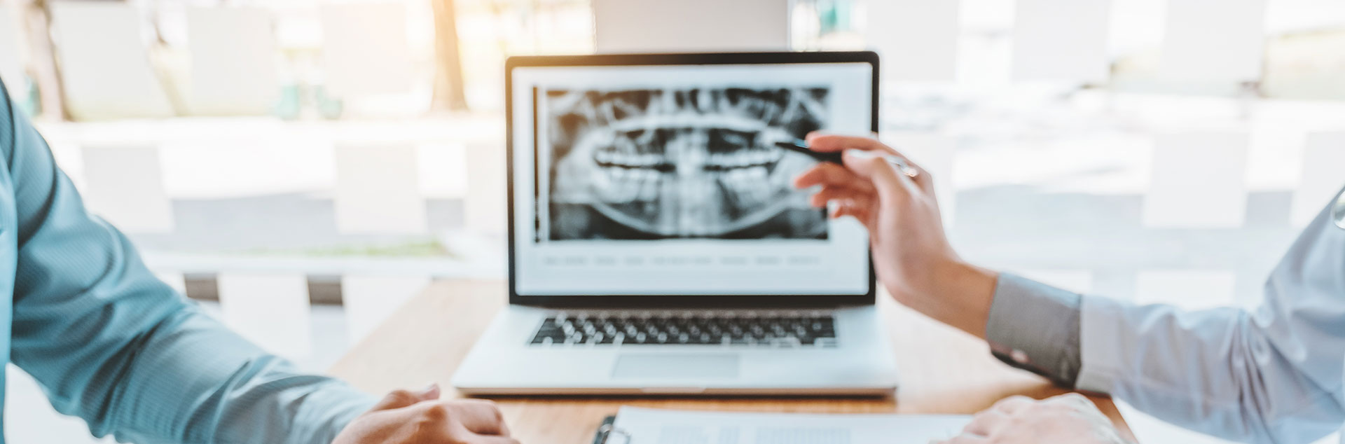 Two professionals engaged in a discussion at a table with laptop, one person gesturing and the other attentively listening.