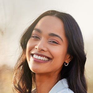 The image is a portrait of a smiling woman with dark hair, wearing earrings and a light-colored top.